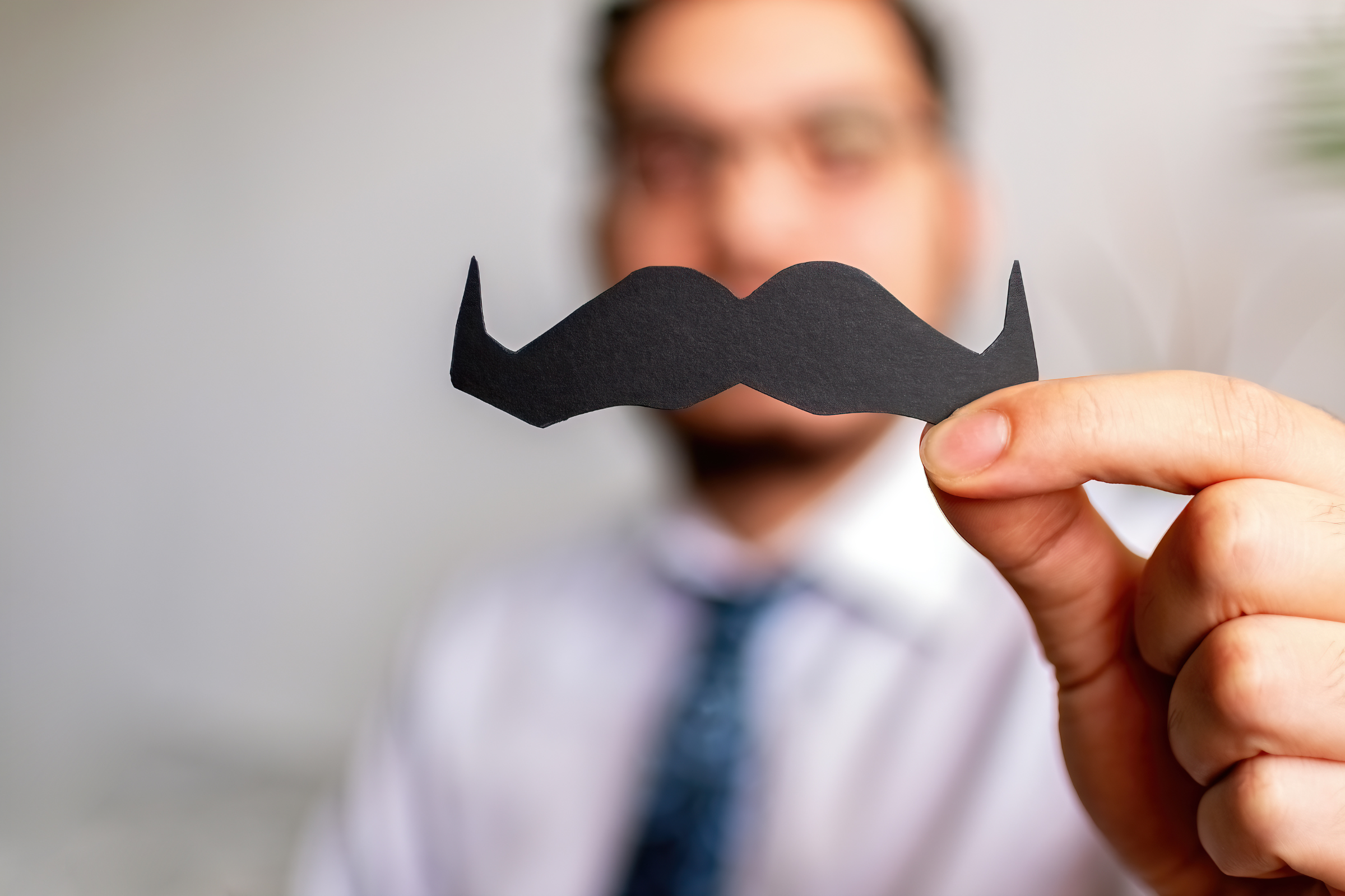 homme en costume tenant dans sa main gauche une moustache découpée dans du papier